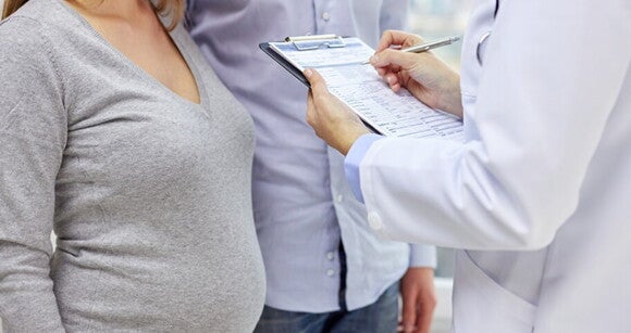 Mulher grávida ao lado do marido sendo avaliada por um médico Mulher grávida ao lado do marido sendo avaliada por um médico