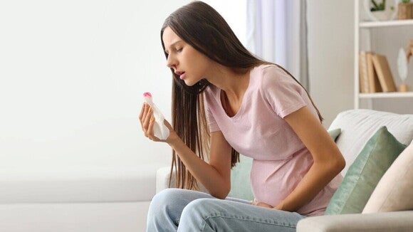 Mulher grávida sentada no sofá, olhando para um lenço de papel sujo de sangue. A mão dela está sobre a barriga. A imagem ilustra o incômodo de ter o nariz sangrando na gravidez.