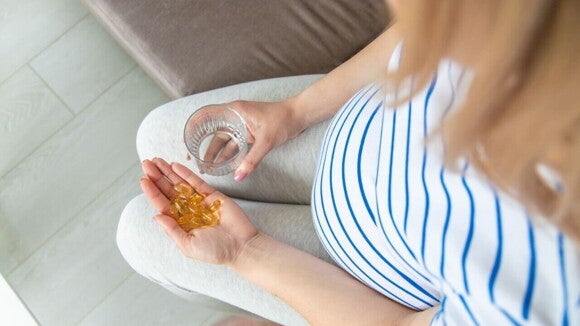 mulher grávida segurando cápsulas de ômega 3 e um copo de água. mulher grávida segurando cápsulas de ômega 3 e um copo de água.