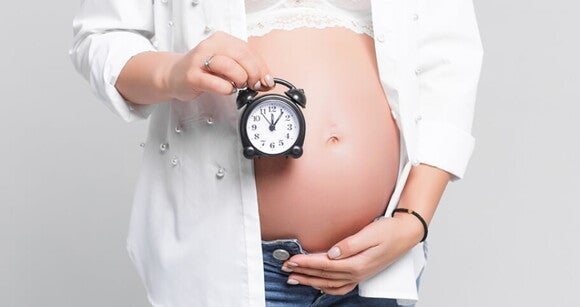 Mulher grávida com a mão sob a barriga e segurando um relógio. Mulher grávida com a mão sob a barriga e segurando um relógio.