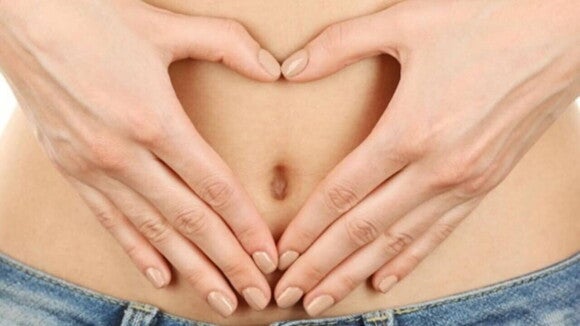 Mãos femininas formam um coração sobre a barriga.