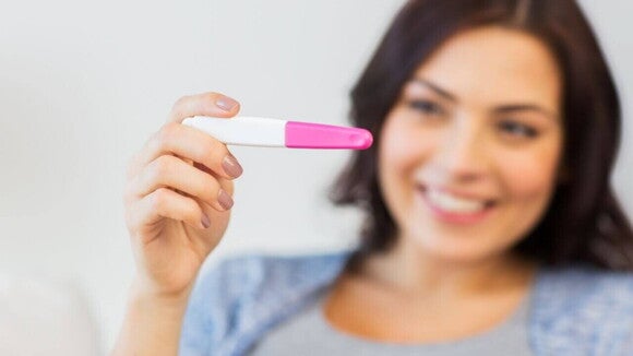 Mulher sorrindo levemente e segurando um teste de gravidez, representando a alegria após um resultado positivo.