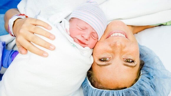 Close-up de uma mãe sorridente e feliz após o parto, com seu recém-nascido enrolado.